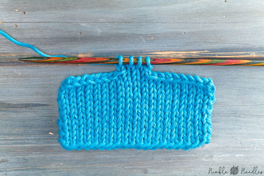 a swatch bound off symmetrically on both sides in blue yarn on a wooden table