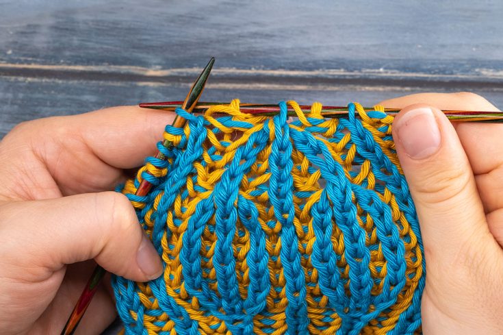 someone showing how to knit brioche double decreases in contrasting yarn
