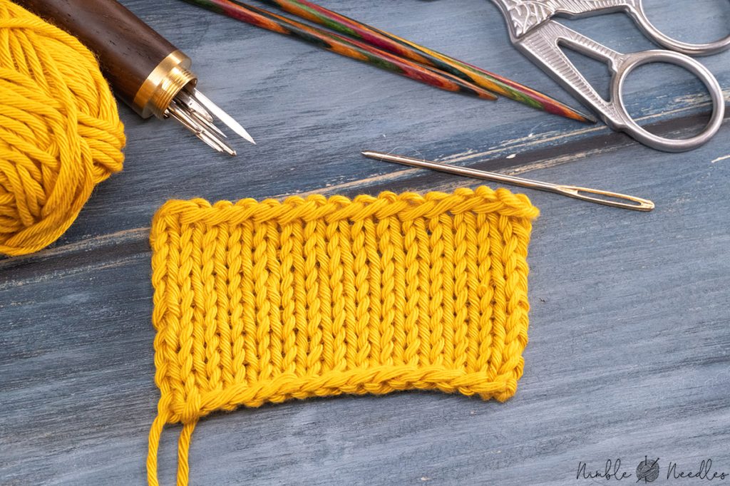 swatch with longtail bind-off edge on a table and various knitting tools in the background