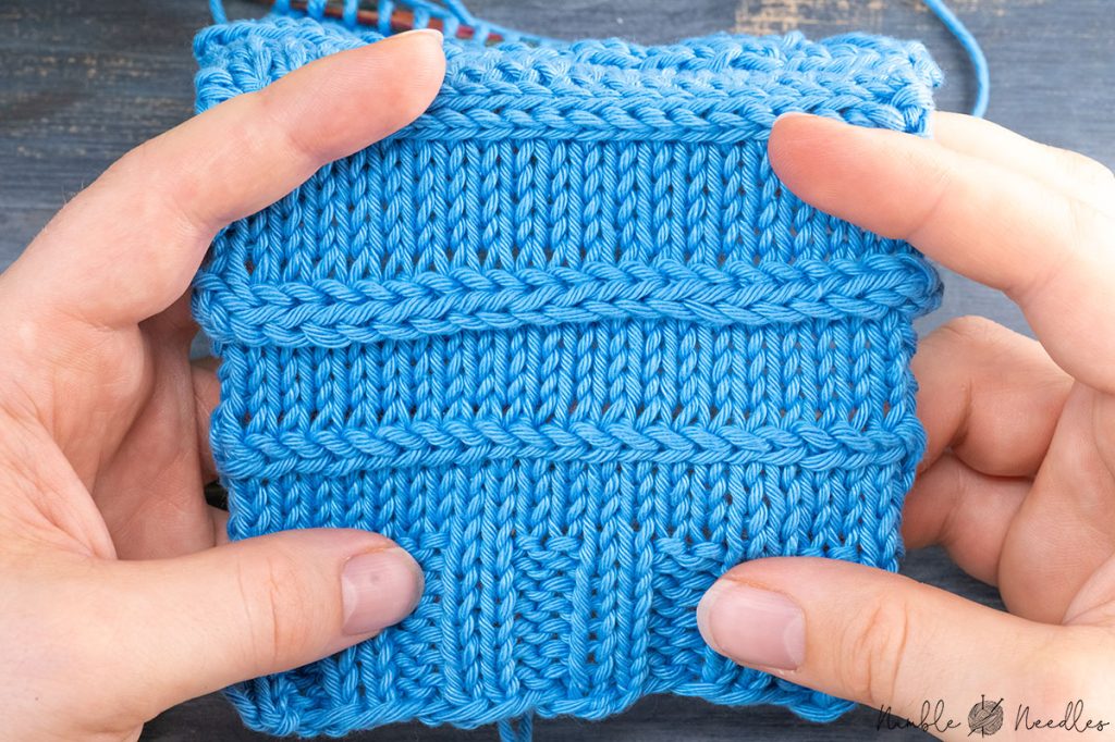someone holding a swatch with horizontal cables in blue yarn